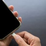 Finger plugging a charger Mobile on Black wood background