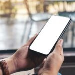 Mockup image of woman's hands holding black mobile phone with blank desktop screen